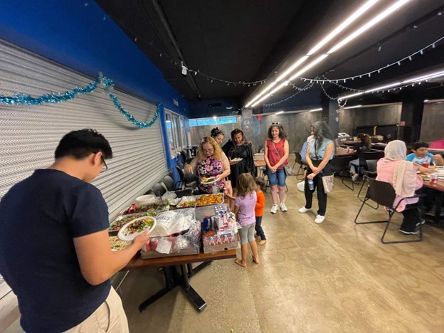 U of T Student Volunteers and community members enjoying Syrian cuisine catered by a newcomer kitchen at the Cat’s Eye in their Cultural Exchange Workshop